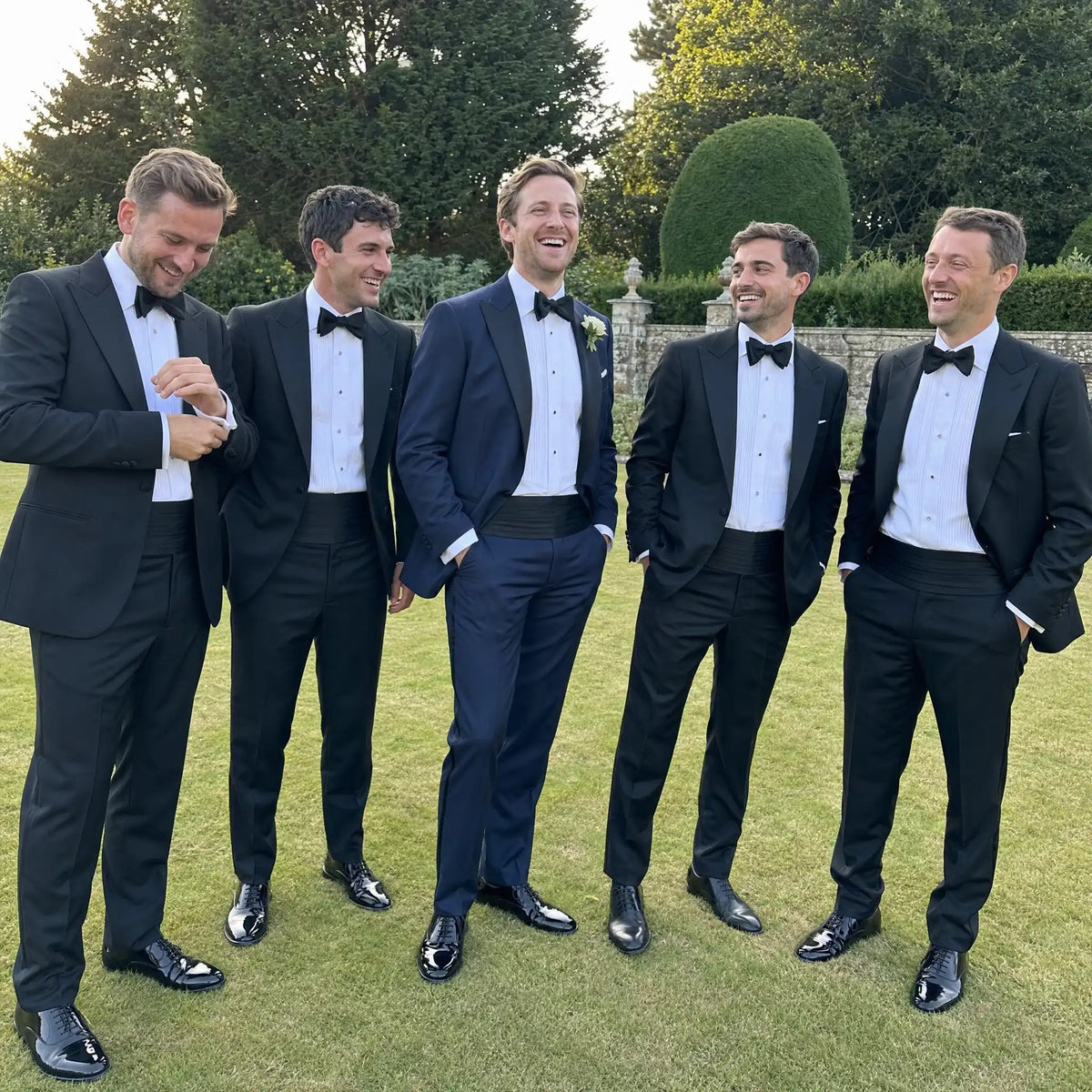 Groom and groomsmen in dinner suits with cummerbunds at a black tie garden wedding